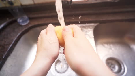 slow motion shot of female hands washing a potato under water from a kitchen tap