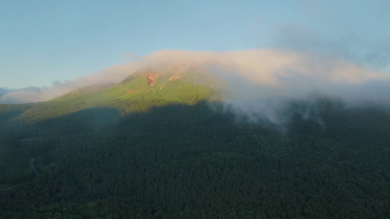 Aerial fly through clouds at dawn in Hokkaido’s Onneto forest mountains, Japan landscape reflecting Ainu heritage and summer stillness