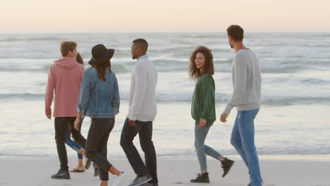 group of friends walking along winter beach together