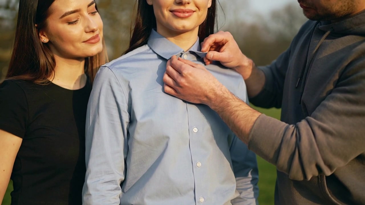 Hombre con sudadera gris ajustando el cuello de la camisa azul claro de la mujer central después de posar en grupo en el parque.
