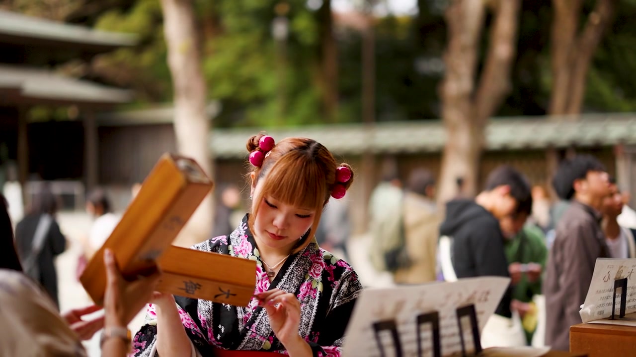 Uma jovem em quimono tradicional agita uma caixa de sorte de madeira no Santuário Meiji, Tóquio