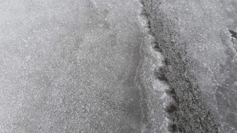 aerial - frozen lake in cold winter, ice with cracks, top down wide shot forward