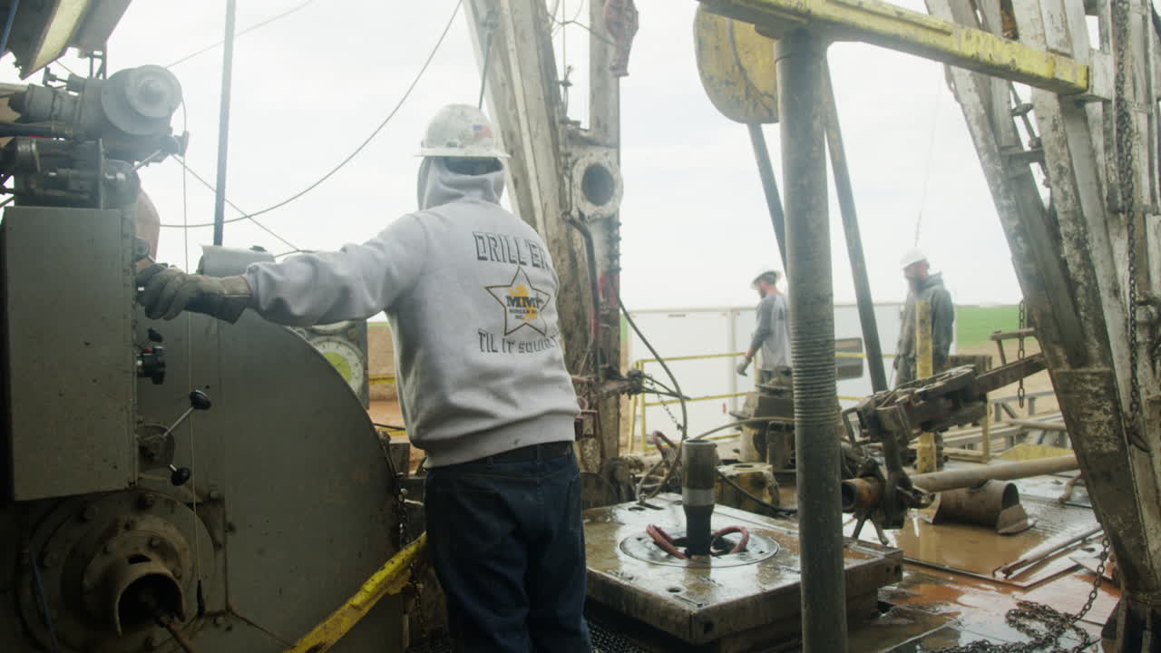Equipment at the site for oil and gas production. Few men wearing protective helmets work at the location.