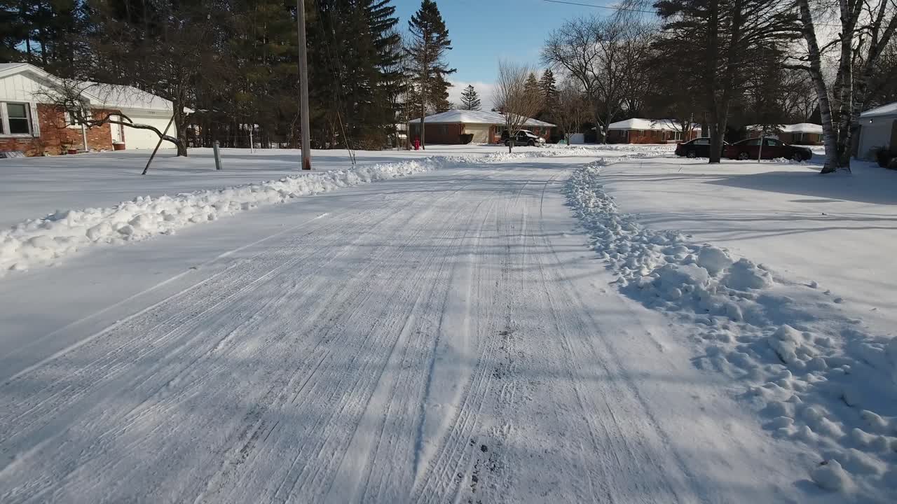 A forward driver's point of view of a snow covered residential neighborhood road.