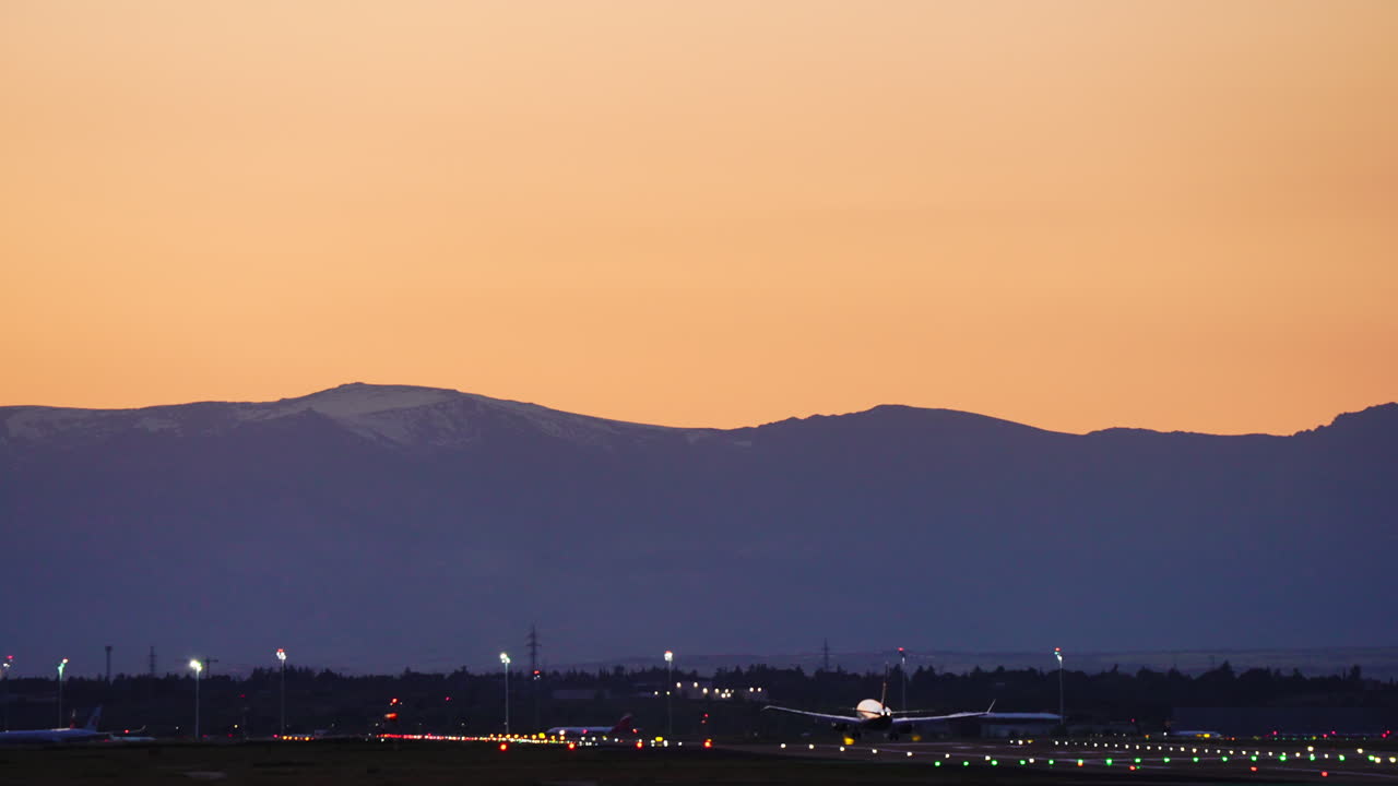 Massive passenger jet descending gracefully toward runway, silhouetted against vibrant sunset colors with mountain landscape creating dramatic scenic backdrop