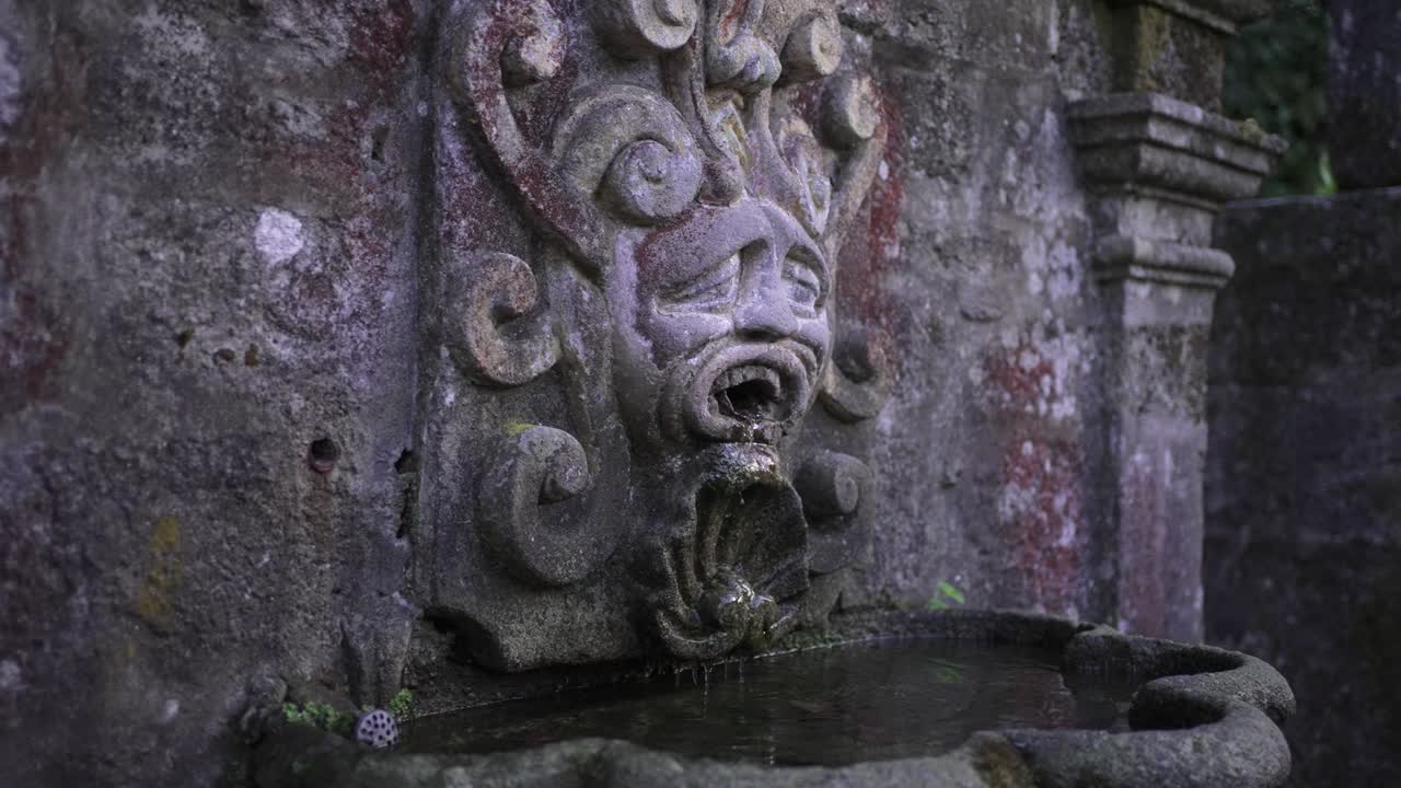 Weathered stone fountain with carved face spout water trickling into basin below