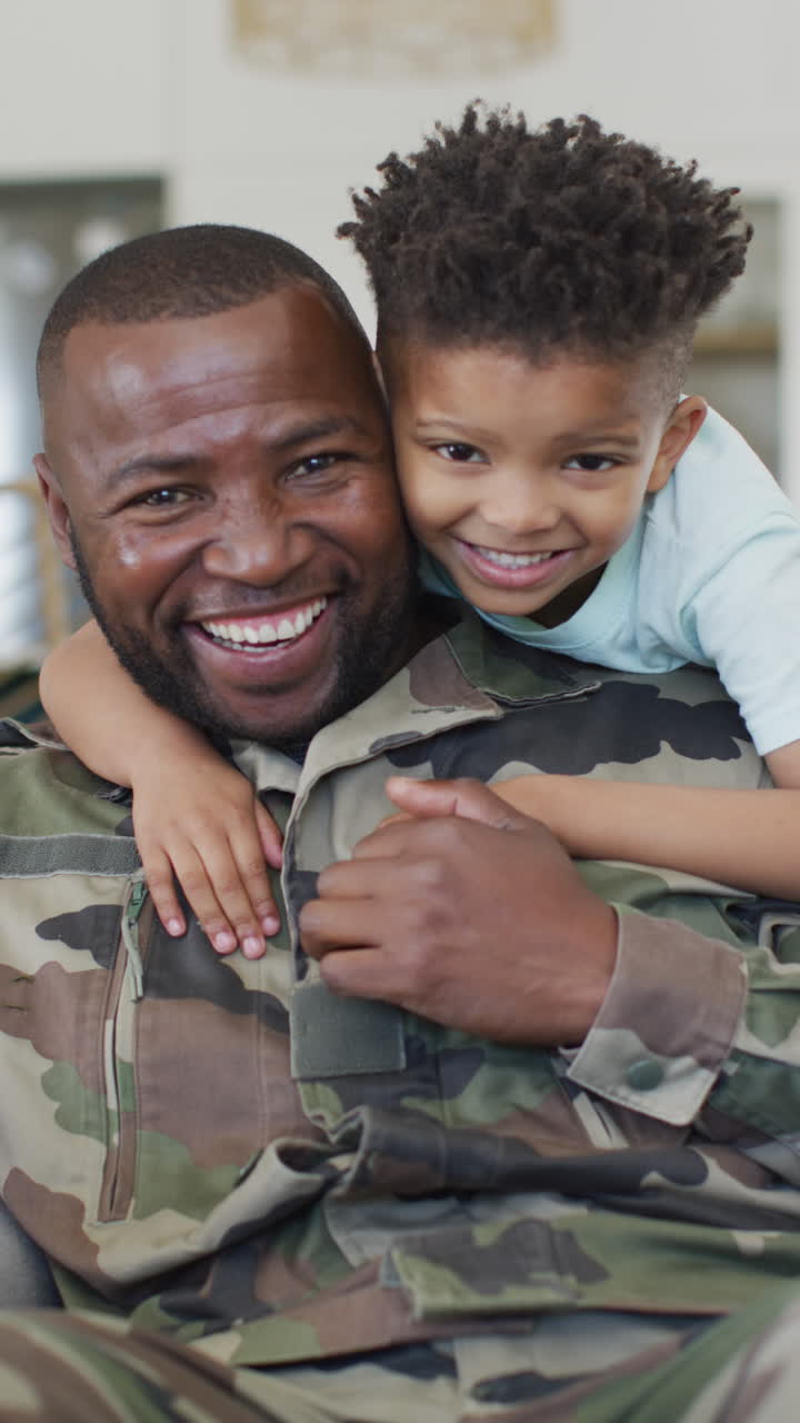 Vertical video of portrait of african american male soldier and his son embracing