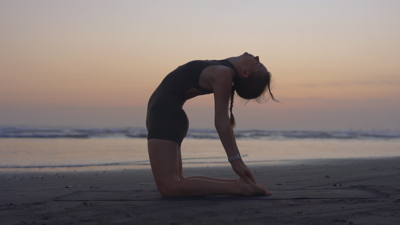 kvinde, der praktiserer yoga på stranden ved solnedgang