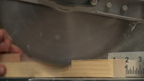 a close-up of a miter saw making a cross-cut of a work piece with sawdust flying. a hand is taking cut work piece