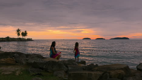 mother and daughter bonding moments on rocky waterfront of kota kinabalu at sunset in sabah, malaysia