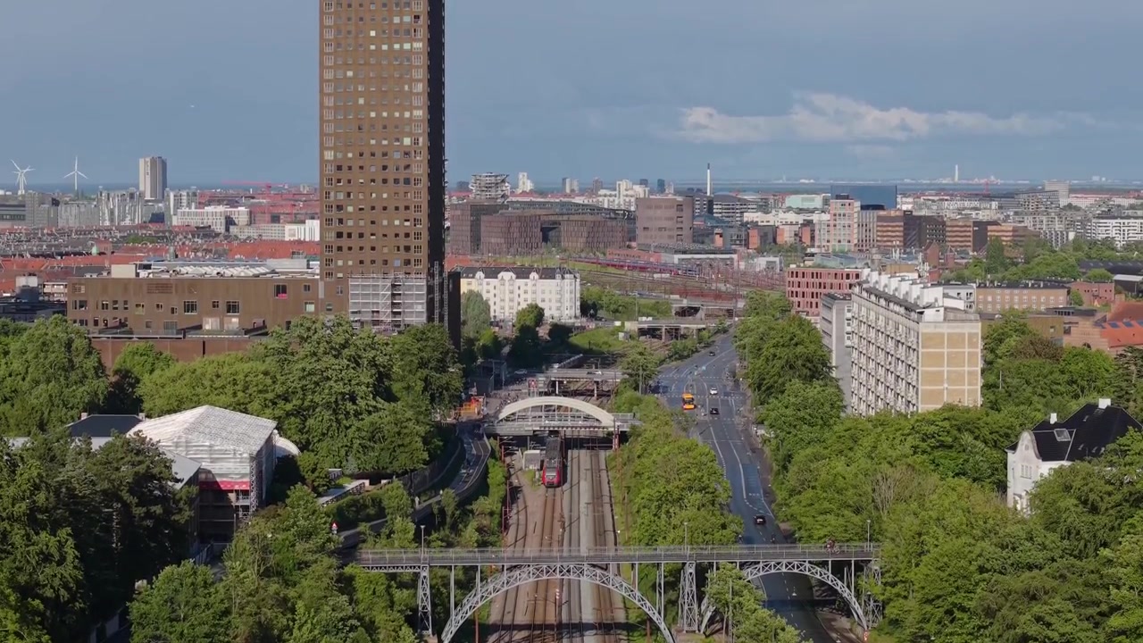 Filmagem aérea de drone seguindo um trem em movimento por Copenhague, exibindo a arquitetura colorida da cidade, infraestrutura ferroviária, telhados e o ambiente urbano dinâmico