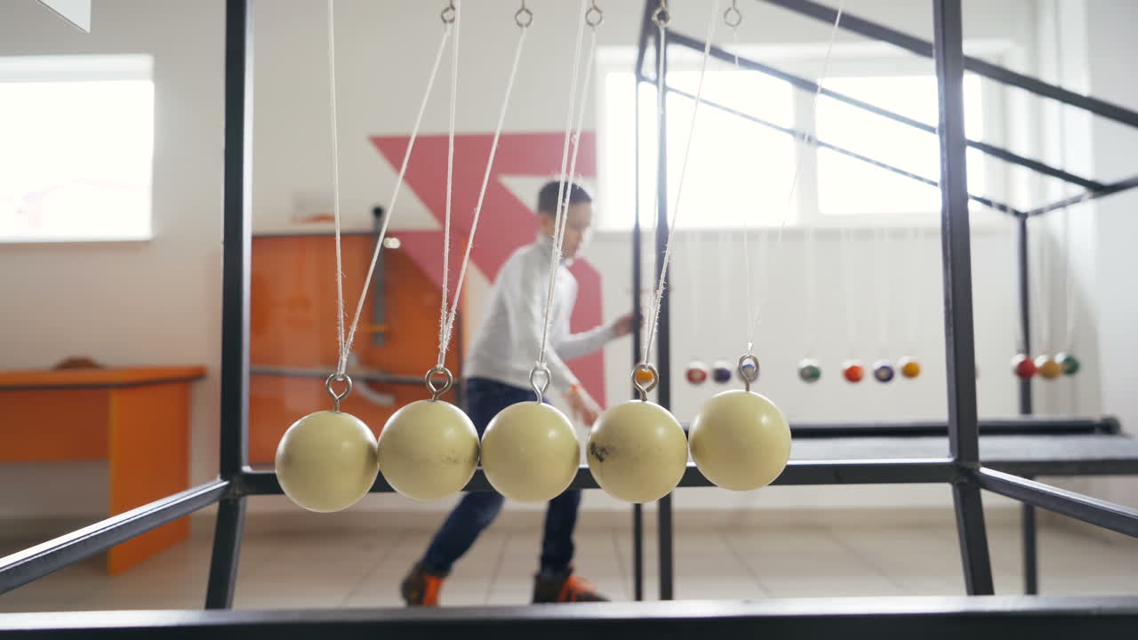 Boy makes an experiment with Newton's pendulum. The concept of physics. Museum of Science