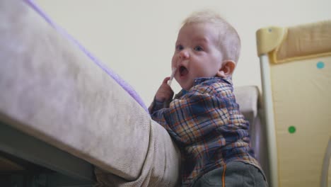 little-baby-in-warm-clothes-climbs-on-large-soft-bed-in-room