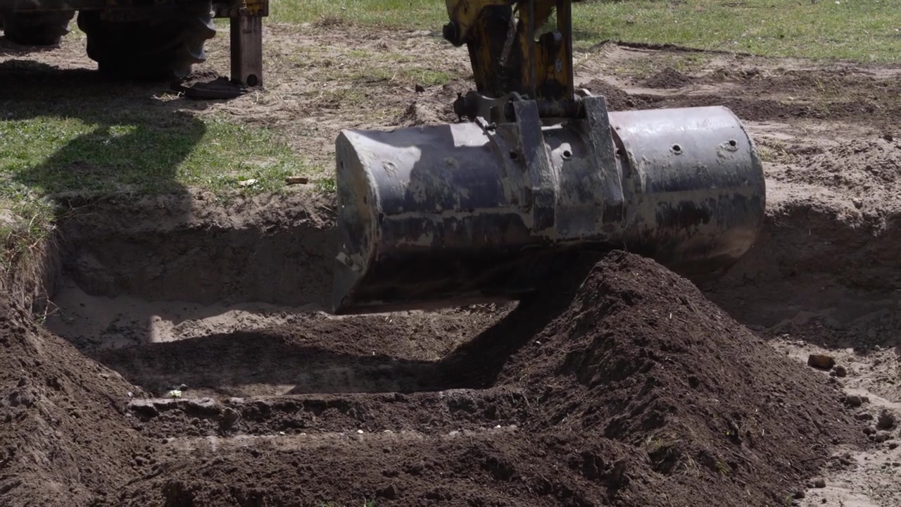 Heavy machinery bucket dumping topsoil while digging a water-storing rain garden for irrigation