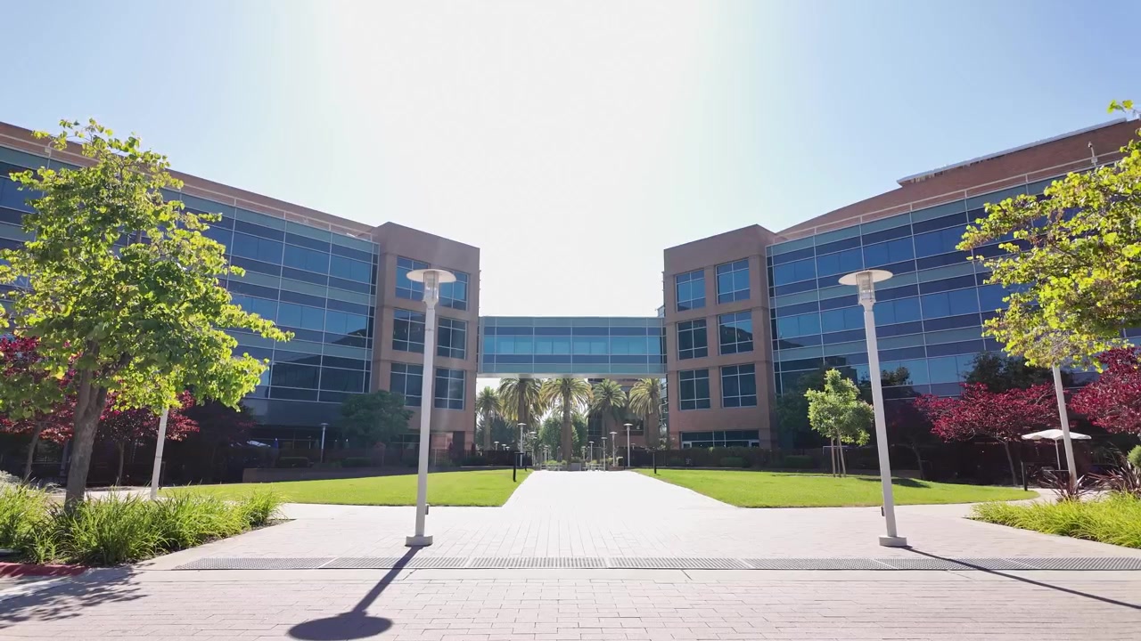 Día soleado y brillante iluminando la moderna arquitectura de cristal de la sede de Google en Silicon Valley, mostrando una pasarela pavimentada y césped verde entre dos edificios de oficinas simétricos