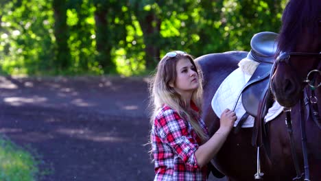 una joven rubia con una camisa a cuadros da un paseo con su caballo. una mujer se comunica con un caballo. noche soleada de verano.