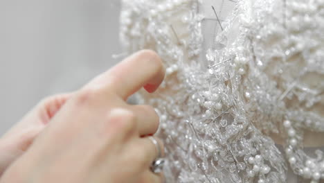 Close-up-fashion-designer-for-brides-in-his-Studio-pins-needles-lace-wedding-dress.-Seamstress-creates-an-exclusive-wedding-dress.-Secure-with-pins-and-needles-outline.-Small-private-business.-Sew-rhinestones-and-crystals-to-the-dress-thread-and-needle.-Jewelry-work.