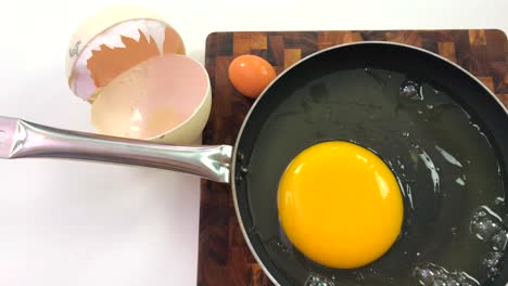 Ostrich-egg-cracked-open-in-a-black-pan-with-big-ostrich-egg-shell-on-the-side,-top-view