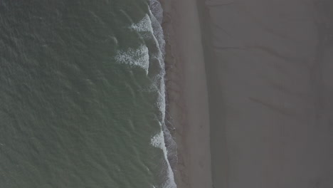 Slow-Aerial-Overhead-Top-Down-Birds-Eye-View-of-Green-Ocean-Water-and-Brown-Beach