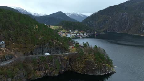 White-minubus-approaching-Stamneshella-village-in-Norway-during-springtime,-aerial