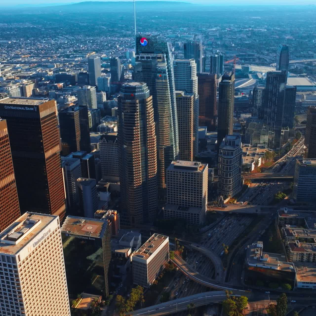 Flying over the stunning skyscrapers in downtown Los Angeles. Multi-lane highway with hundreds of cars passing through the city centre. Aerial view