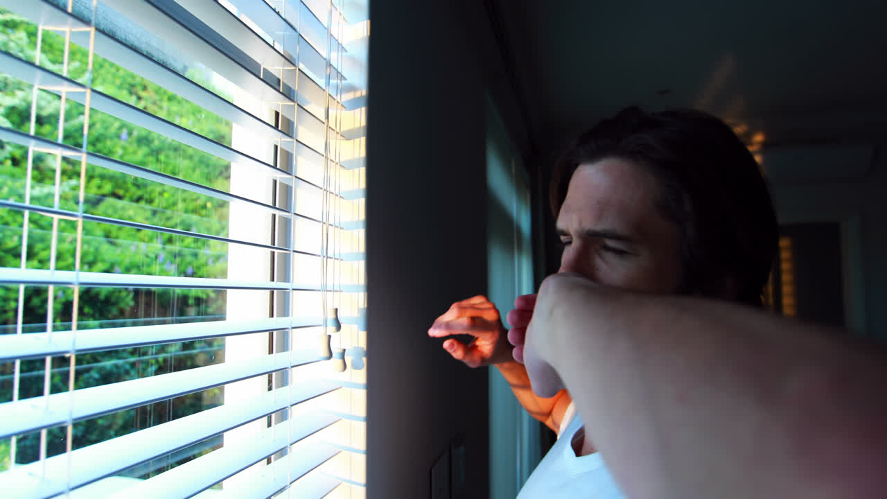 Man looking through window blinds after waking up