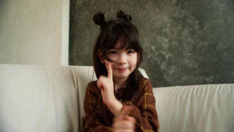 kid girl sitting on sofa, having fun entertaining alone in living room, dancing while sitting