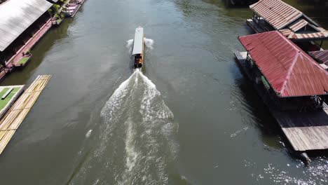 A-longtail-boat-is-sailing-on-a-river-in-Sai-Yok-National-Park,-passing-by-a-very-charming-floating-village-in-the-middle-of-the-jungle-of-Thailand-in-Southeast-Asia