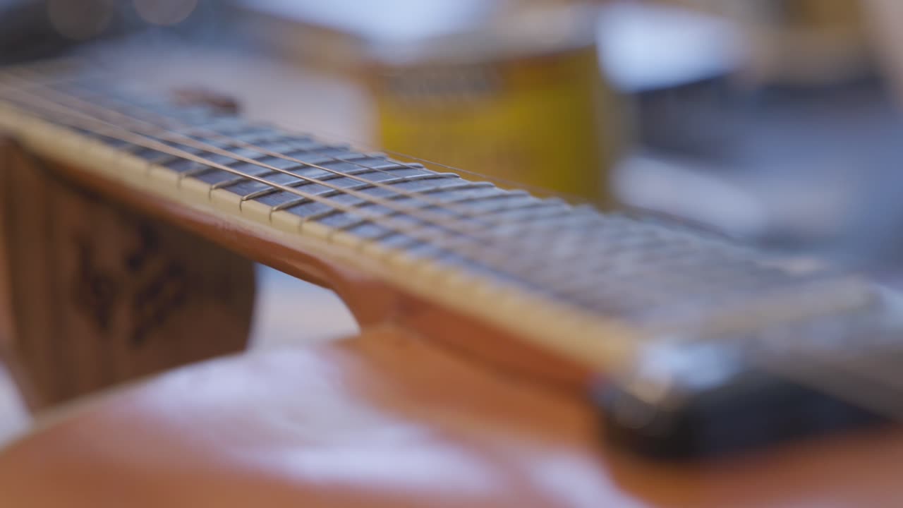 Slow motion footage panning down the length of the neck of a guitar that has strings on it.
