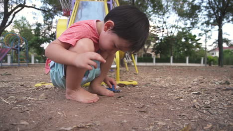 east asian boy kid using his imagination and having fun on his free time  playing at a park with toy cars while squatting on the floor