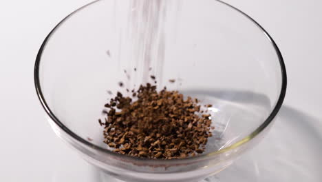 grains of coffee being poured into a small glass bowl in a slow-motion shot