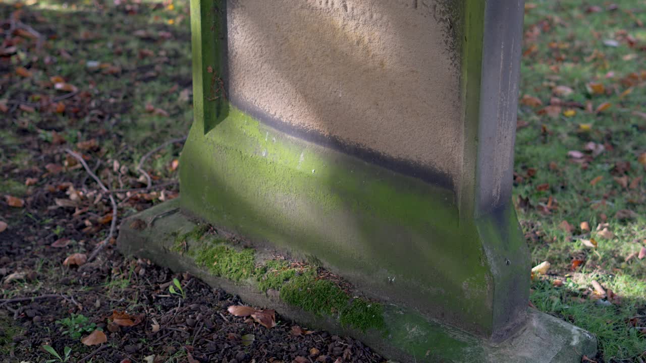 Weathered gravestone with moss in an old cemetery surrounded by autumn leaves in Northumberland