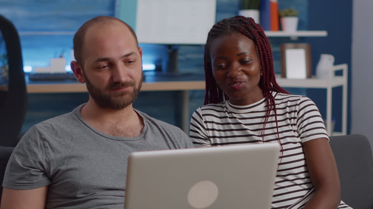 Young interracial couple waving at video call camera on laptop