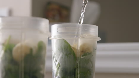 mano de mujer vertiendo agua en una taza de batido antes de mezclar en cámara lenta