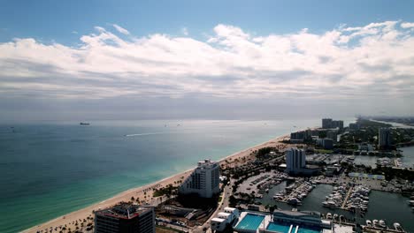 Impresionantes-Imágenes-Aéreas-De-Playa-Y-Arena-Con-Aguas-Tranquilas,-Edificios-En-El-Costado,-Agua-Azul,-Cielo-Azul,-Palmeras,-Pies.