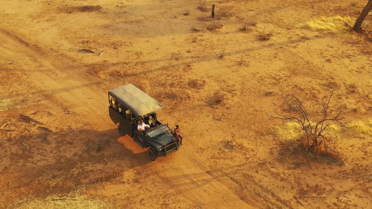 excelente vista aérea de un jeep safari que viaja por las llanuras de áfrica en la reserva de caza de erindi, namibia, con un guía nativo de observación tribal de san sentado en la parte delantera observando la vida silvestre 2