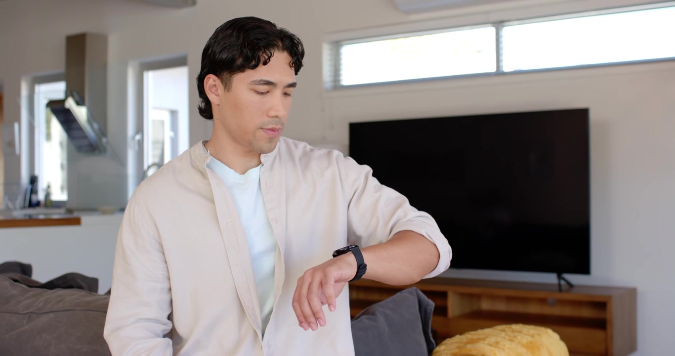 African American man sitting on couch at home glancing up, checking smartwatch for notifications