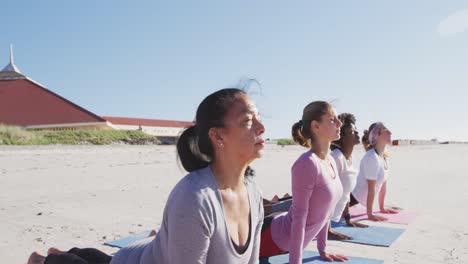 Multiethnische-Gruppe-Von-Frauen,-Die-Yoga-Position-Am-Strand-Und-Im-Hintergrund-Des-Blauen-Himmels-Machen