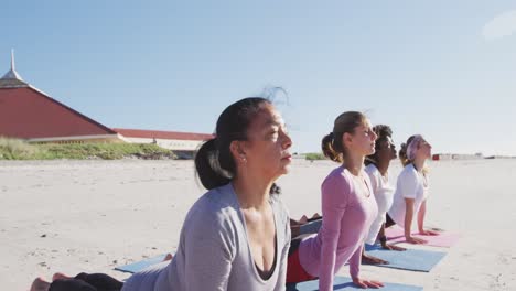 Multi-ethnic-group-of-women-doing-yoga-position-on-the-beach-and-blue-sky-background