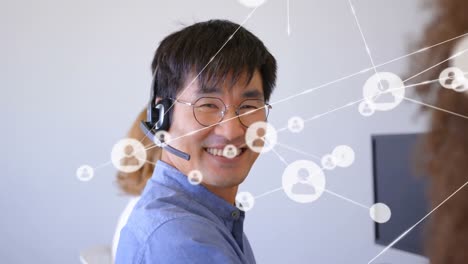 Animation-of-network-of-profile-icons-over-asian-man-wearing-phone-headset-smiling-at-office