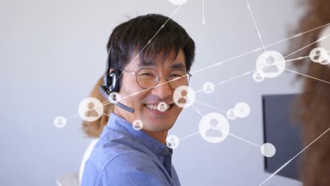 animation of network of profile icons over asian man wearing phone headset smiling at office