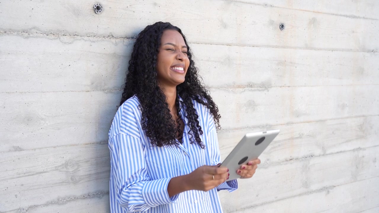 A woman using a tablet while relaxing in a casual setting against a concrete background