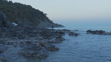 Man-fishing-along-rugged-island-shoreline-Wide-Shot