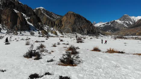 two people in a snow taking pictures with a big dslr camera and telephoto zoom lens. sunny day in winter. annapurna conservation area, manang valley, nepal. aerial drone shot going forward.