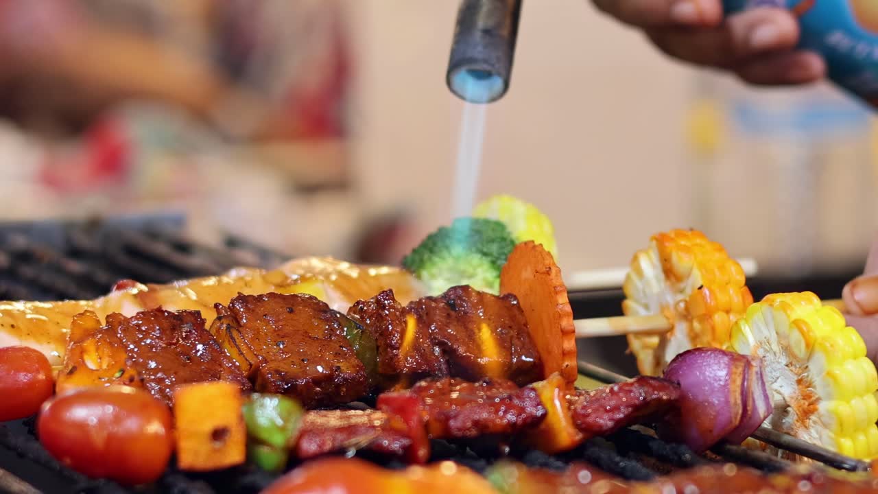 Primo piano di spiedini con verdure e carne grigliati usando un cannello.