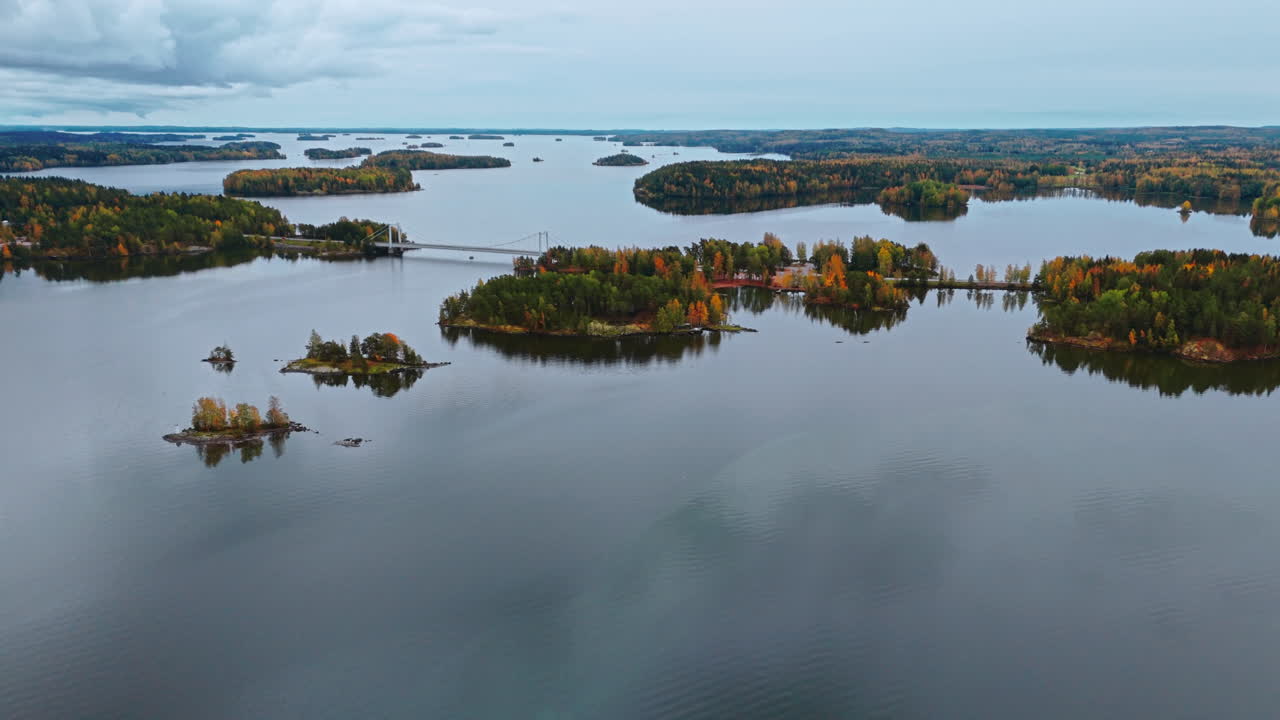Approaching a bridge crossing a huge lake and it's archipelago islands surrounded by an autumn forest with red, green yellow and brown trees