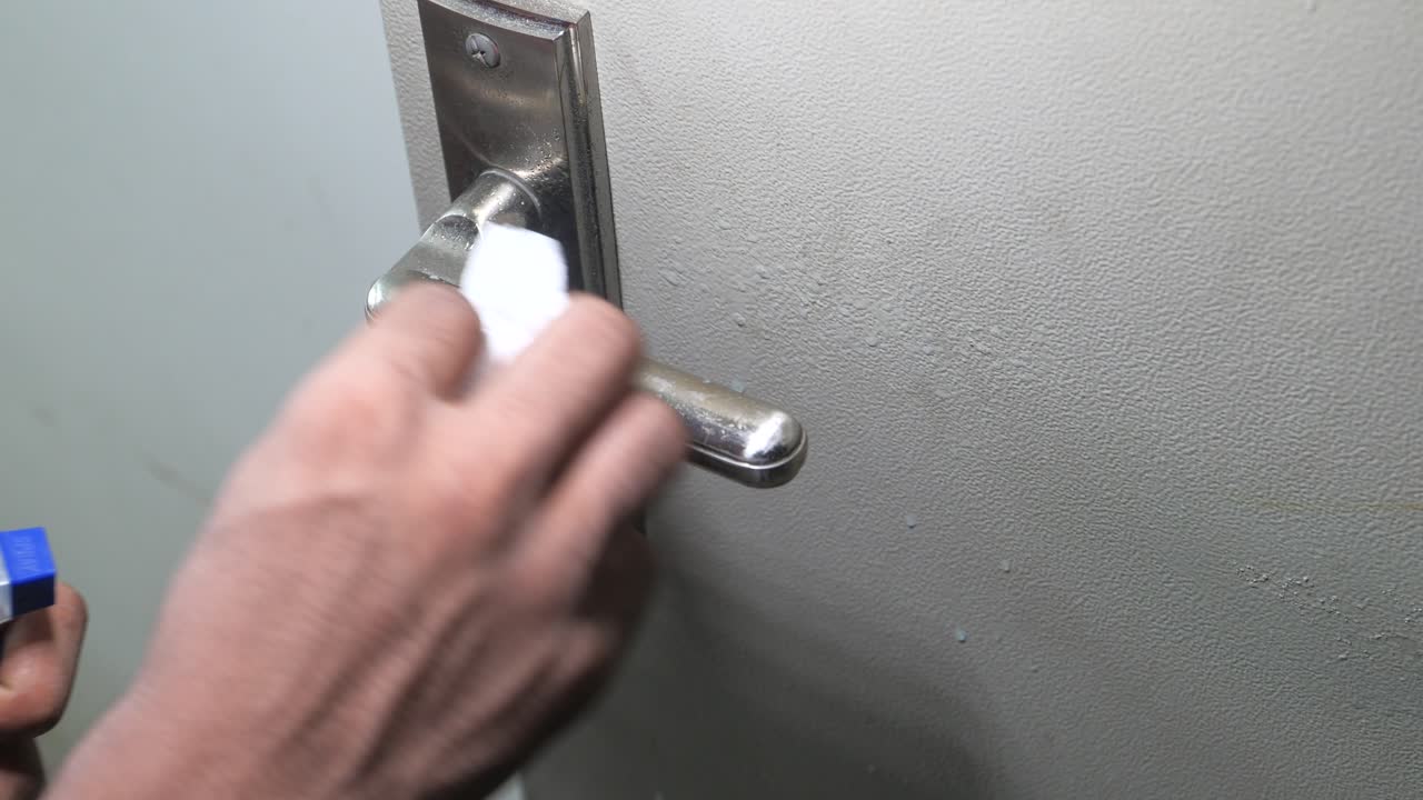 limpieza de una manija de la puerta con una botella de spray y una toalla