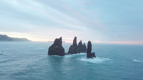 reynisdrangar rocks at reynisfjara beach next to vik i myrdal at south iceland. aerial drone shot flying over a cliff during sunrise. large storm waves crash rock. high resolution footage. 4k