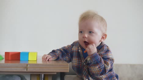 un niño divertido mordisquea un juguete naranja apoyado en una mesa de madera
