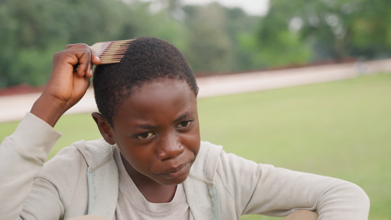Bambino che si pettina all'aperto. Ragazzo che si sistema i capelli pacificamente fuori. Bambino che si pettina e si acconcia i capelli pacificamente all'aperto nella natura. Un giovane ragazzo trascorre un momento tranquillo sistemandosi i capelli all'aperto all'aria fresca.